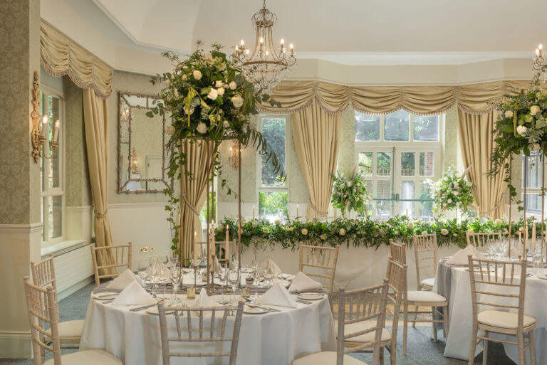 A room set up for a wedding breakfast with large white floral arrangements
