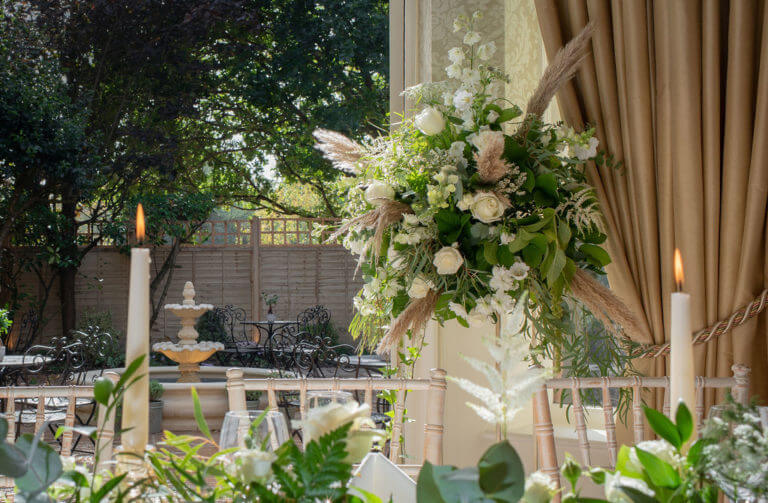 Detail of a flower arrangement for a wedding breakfast with foliage, white roses and pampas grass in a high stand.