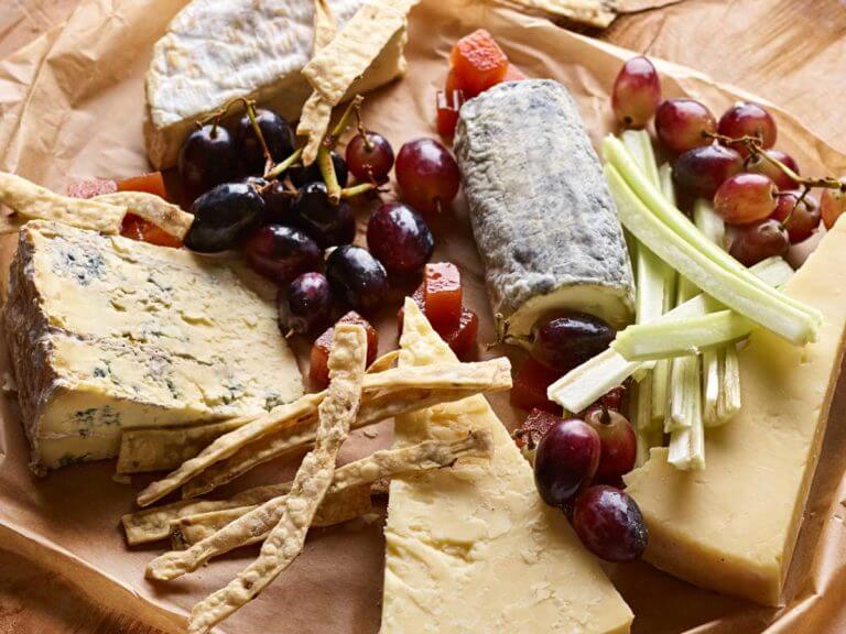 Selection of French cheeses with grapes, celery and breadsticks served on baking paper