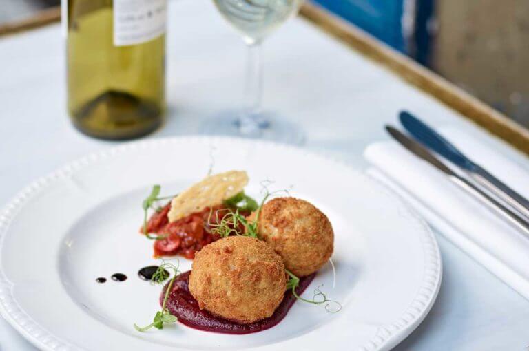 Dish of French food served with bottle of white wine at Le Blaireau French bistro at Careys Manor Hotel & SenSpa outdoor dining