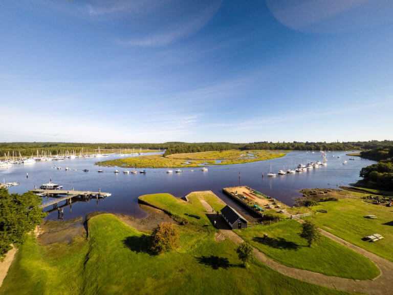 Aerial view of Beaulieu river in the New Forest with sailing boats on the water and a bright blue sky.