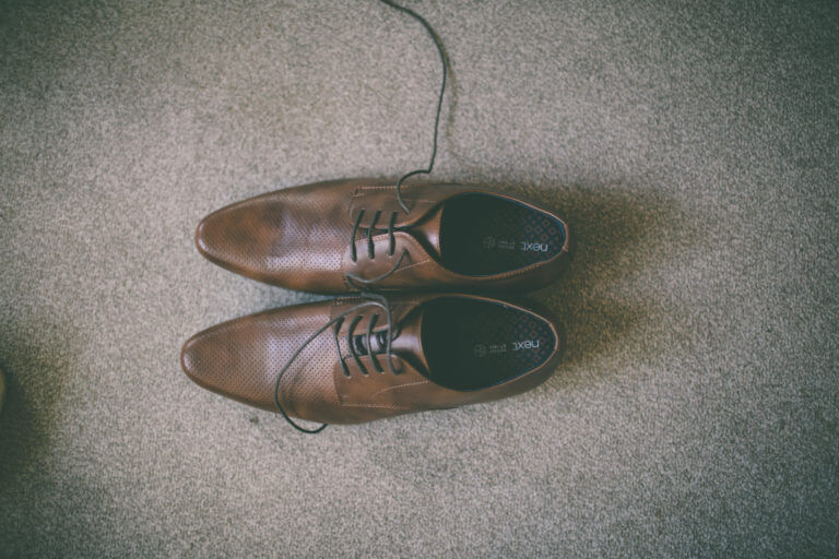 A pair of unlaced men's brown brogue shoes on beige carpet