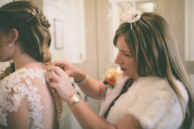 Mother of the bride fastening the buttons on the bride's wedding dress.