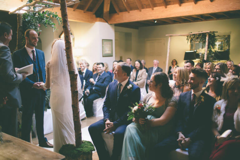 A couple saying their vows in front of all their friends and family during a wedding ceremony in the lounge at Careys Manor.