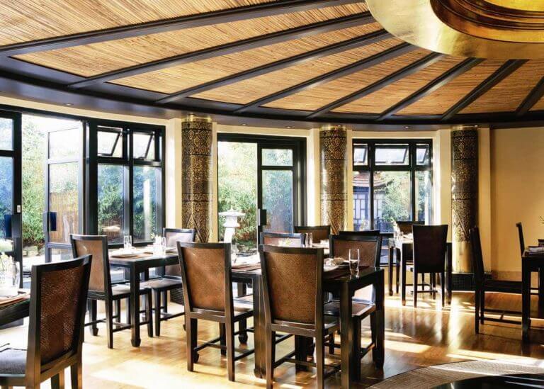 Interior of Zen Garden restaurant at Careys Manor Hotel & SenSpa with decorative gold pattern pillars, bamboo ceiling details, rattan detail chairs and tables