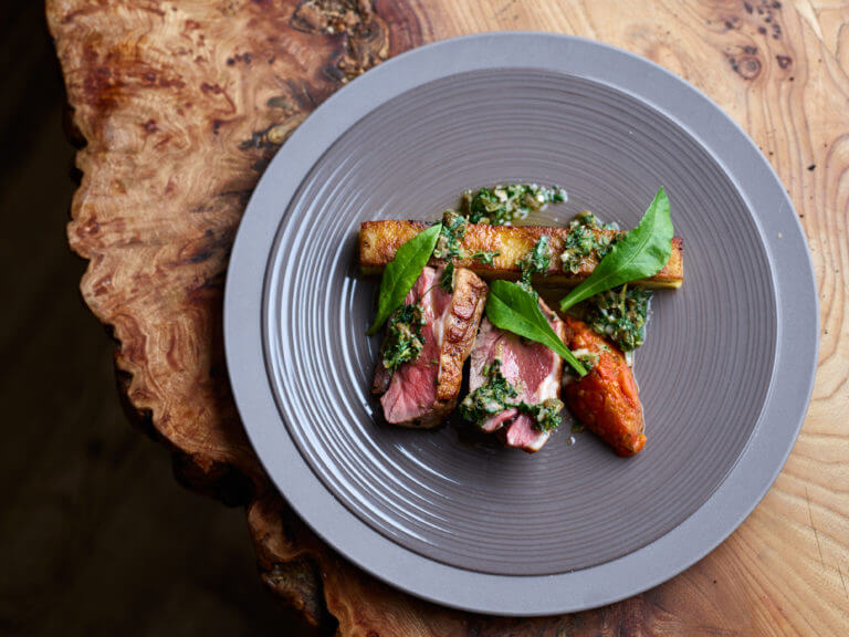 Dish of red meat with potato, green chimichurri and herbs served on wooden table