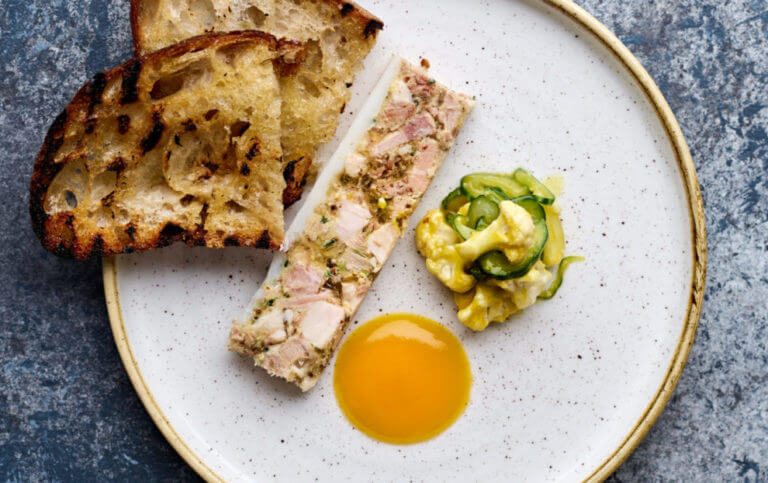Terrine dish served with pickled cauliflower and cucumber, mustard sauce and two slices of sourdough bread