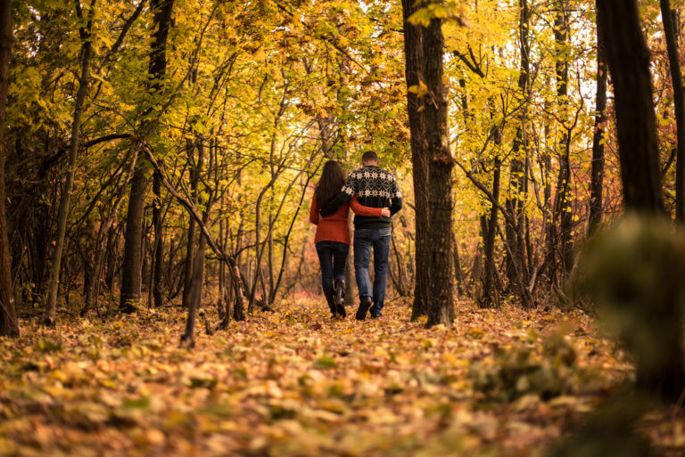 Couple walk through forest in autumn, autumn leaves cover the floor and trees