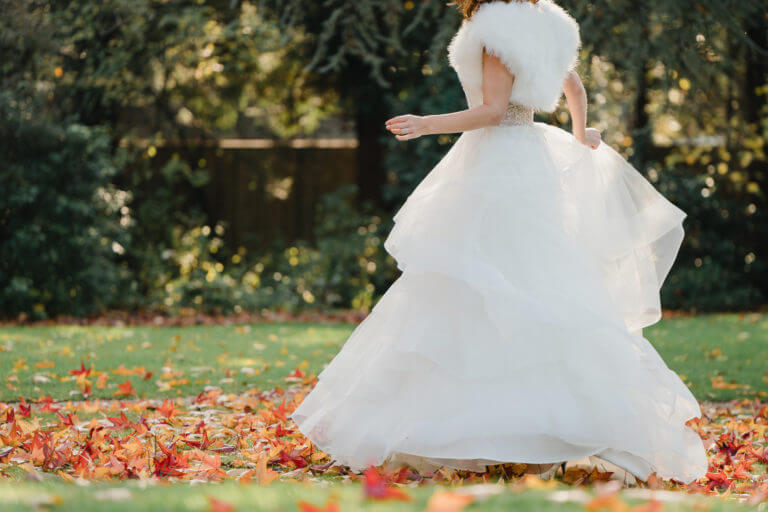 A bride wearing a white fur wrap and voluminous tulle skirt dancing in the autumn leaves.