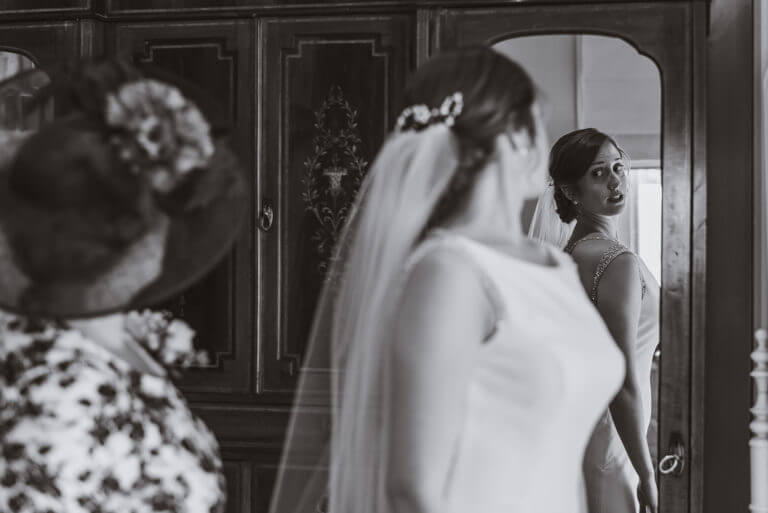 Black and white photo of bride looking over her shoulder into mirror admiring wedding dress
