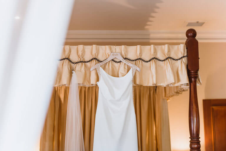 White wedding dress and veil hanging from four poster bed frame