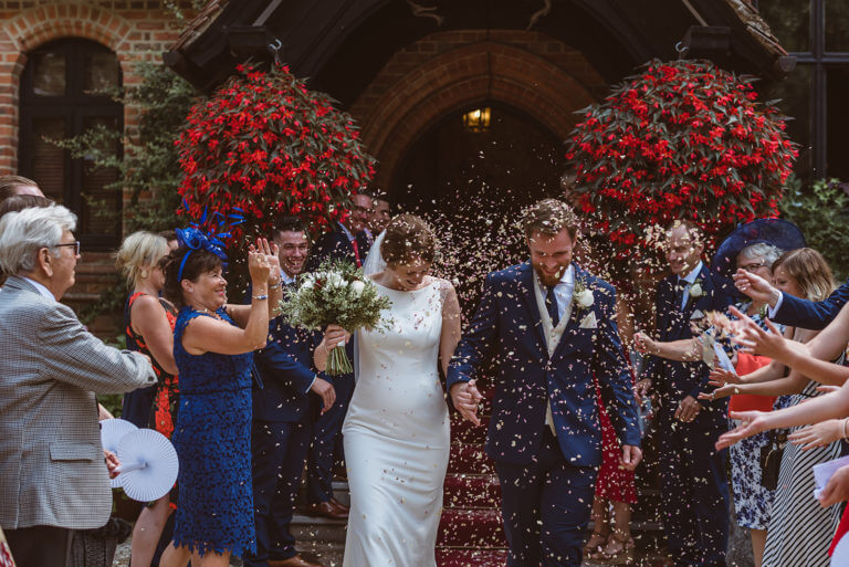 Bride and groom are celebrated with confetti thrown as they leave hotel wedding venue Careys Manor Hotel through main entrance