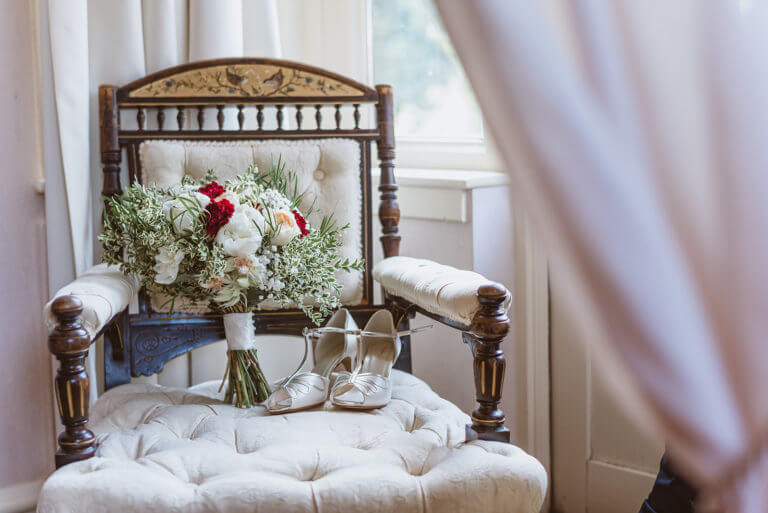 Wooden armchair with cream cushions with bridal bouquet and wedding heels resting on the seat