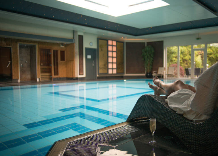 Woman sitting on lounger in white waffle material robe next to swimming pool in spa. Girls' retreat at spa.