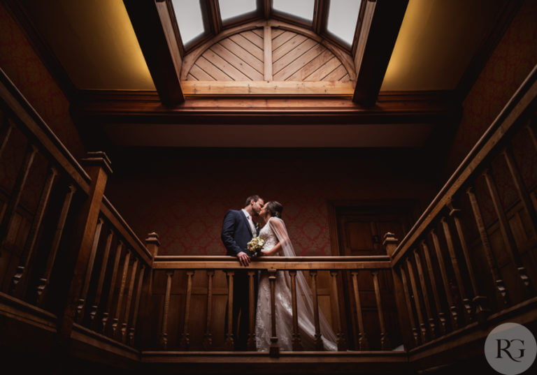 Bride and groom kiss at top of wooden staircase in hotel wedding venue Careys Manor Hotel & SenSpa