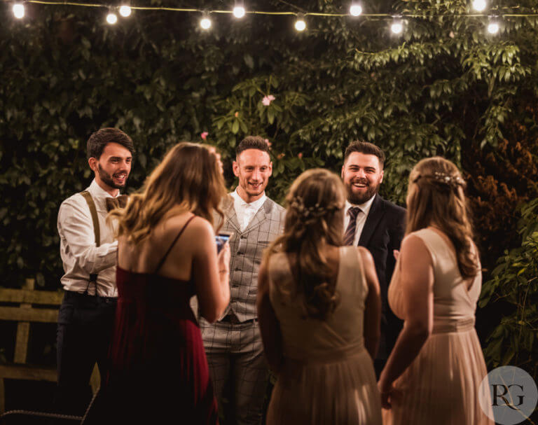 Guests at a wedding chat happily outside after dark under string lights