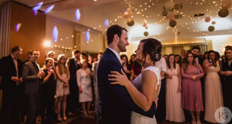 Bride and groom dance together at wedding party with guests looking on happily