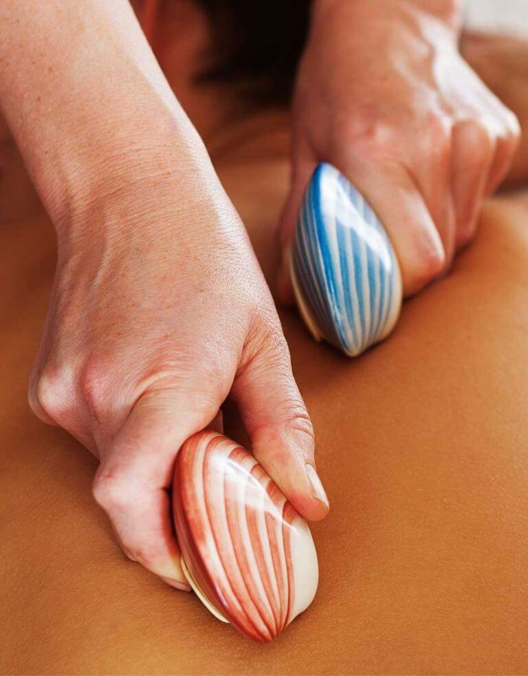 two shells are rubbed along a person's bare back during lava shell massage spa treatment