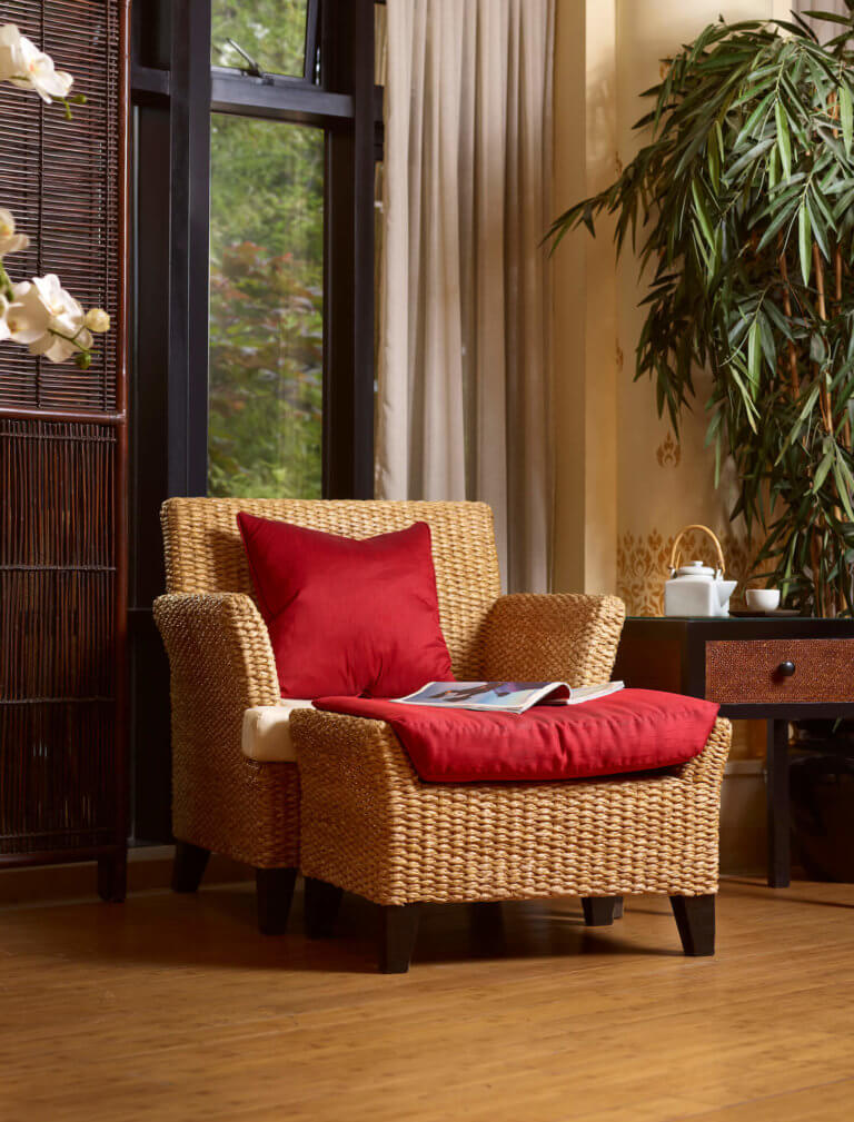 A wicker lounge chair and foot stool with red Thai silk cushions.