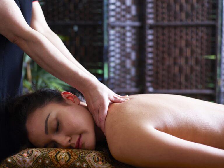 Woman lying on front on massage table receives shoulder massage from spa therapist