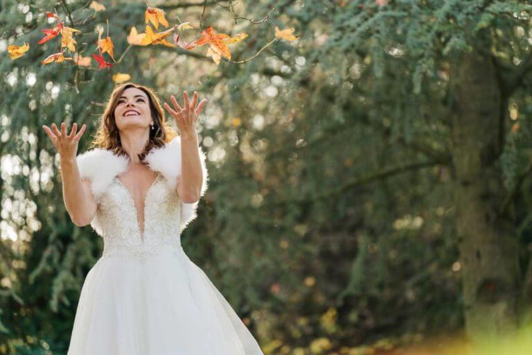 Bride throws autumn leaves in the air during photoshoot in grounds of New Forest wedding venue Careys Manor Hotel & SenSpa