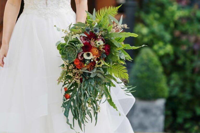Bride holds bouquet of green and red colourful flowers and foliage