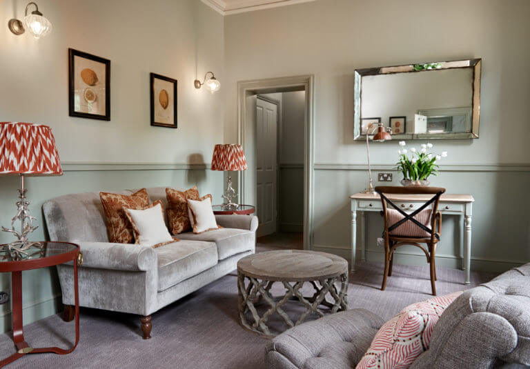 Lounge area of a suite at Careys Manor. Muted grey tones with orange lamps and cushions