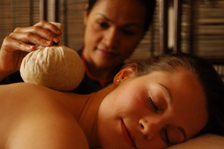Woman receives a Thai herbal poultice back massage by spa therapist