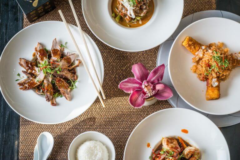 Birds eye view of Thai food dishes served in a restaurant with chopsticks and pink flower