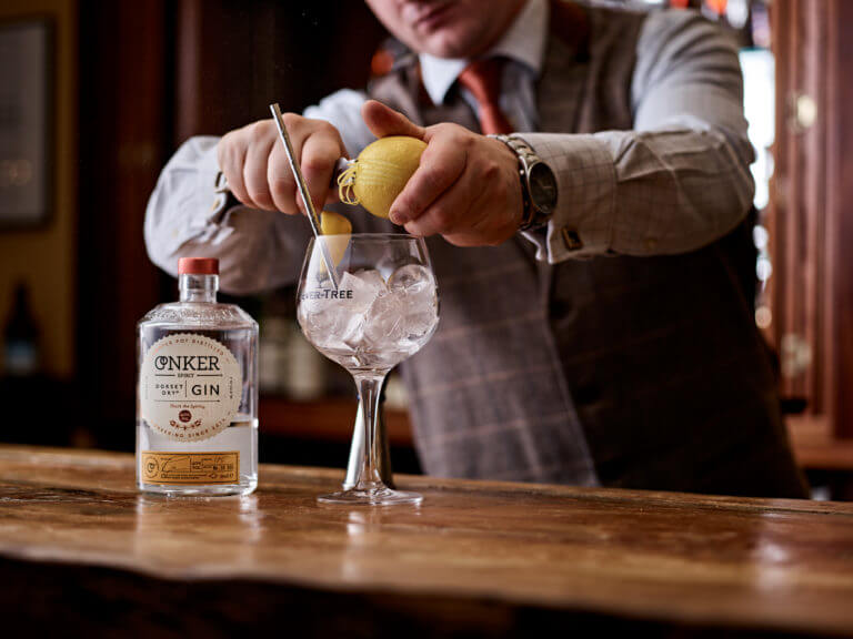 Bartender peeling lemon into into gin glass full of ice