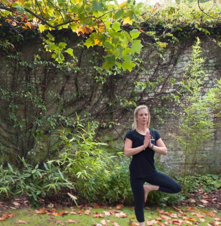 Woman stands in tree pose practicing yoga outdoors surrounded by trees