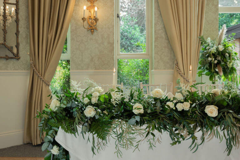 Long table dressed with greenery and cream roses for a wedding at Careys Manor