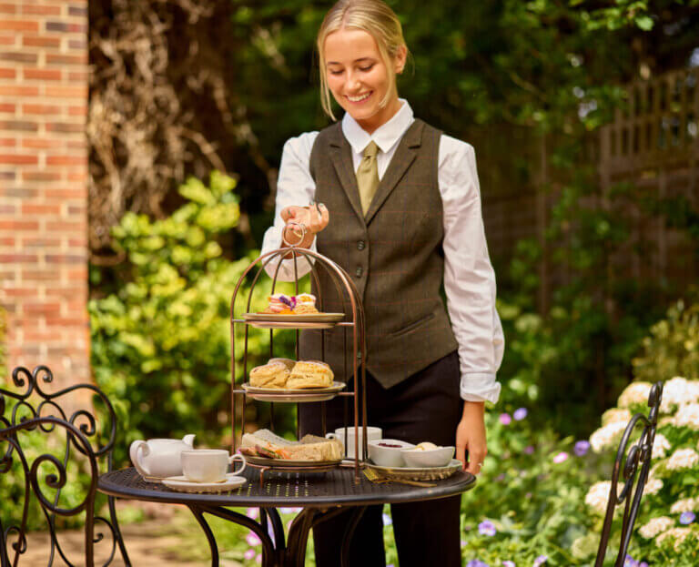 Waitress serving sweet as honey summer afternoon tea on the terrace at Careys Manor Hotel & SenSpa
