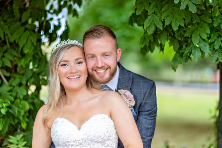 Bride and groom pose happily beneath a tree on wedding day