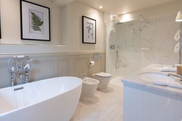 Large bathroom with bath tub, double sink, shower, bidet and toilet in Careys Manor Hotel roof terrace suite