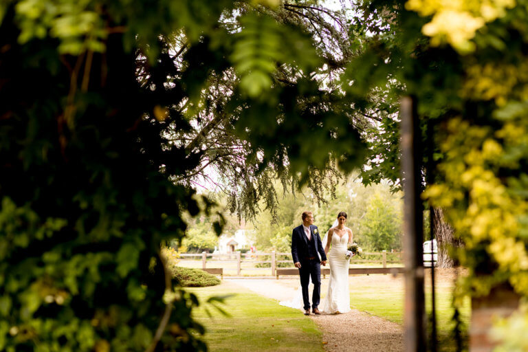 Bride and groom walking hand in hand under trees in grounds of wedding venue