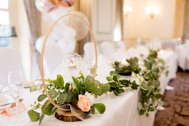 Wooden hoop with hanging tea light over blush roses at the wedding breakfast at Hampshire Wedding venue Careys Manor
