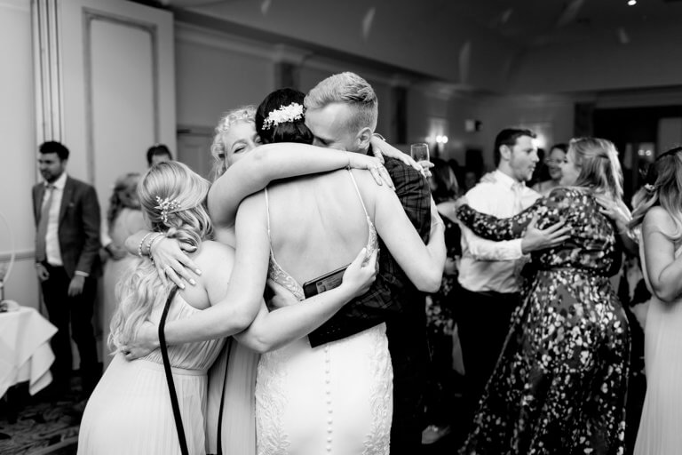 Black and white photo of bride hugging wedding guests on dancefloor at evening reception