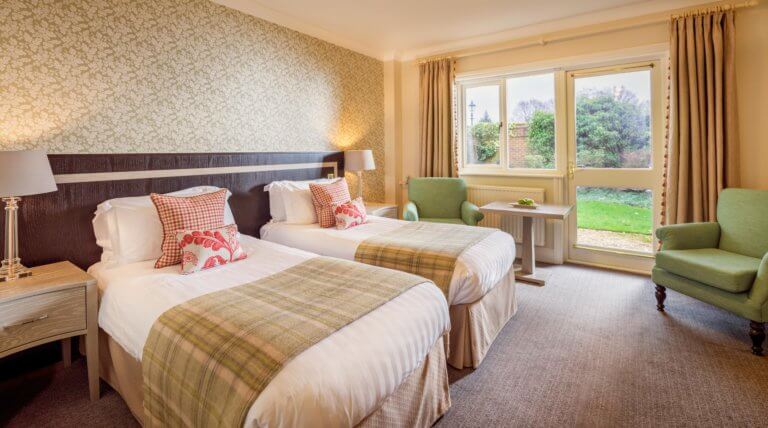 Hotel room with twin beds, two green armchairs, side table with apples on it, door out into garden