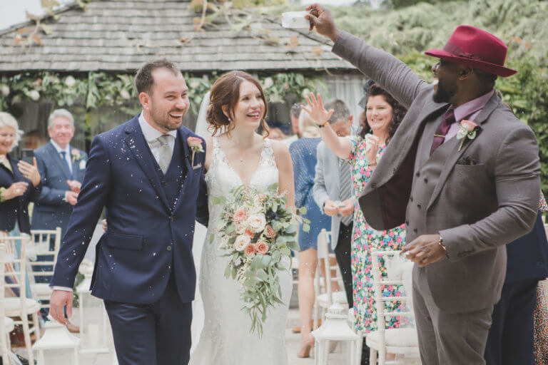 The Bride and Groom walk up the aisle following the ceremony with confetti in the air. at Hampshire wedding venue Careys Manor Hotel