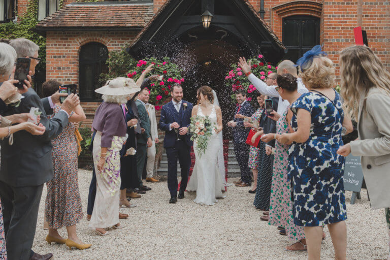 Bride and Groom walk through the centre of their guests throwing confetti outside Hampshire Wedding Venue Careys Manor Hotel