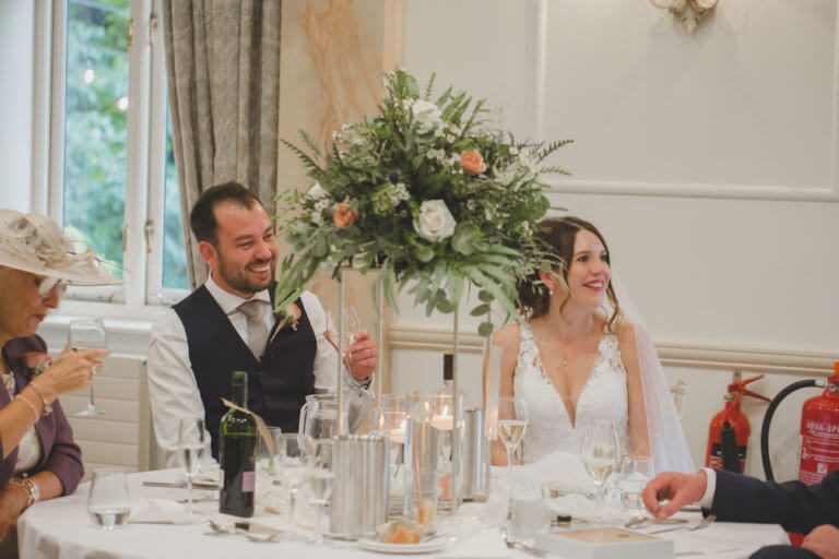 The Bride and Groom smile and listen to speaches during their wedding breakfast at Hampshire Wedding Venue Careys Manor Hotel