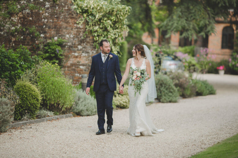 The Bride and Groom walk hand-in-hand up the drive at the front of Hampshire wedding venue Careys Manor Hotel