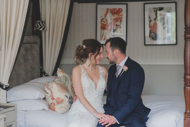 The Bride and Groom sit on the bed gazing into each others eyes at Hampshrie Wedding Venue Careys Manor Hotel