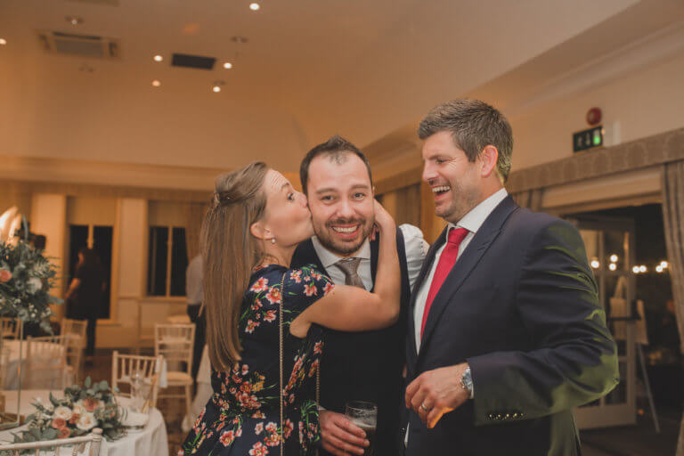 The groom smiles as he receives a kiss from once of his guests