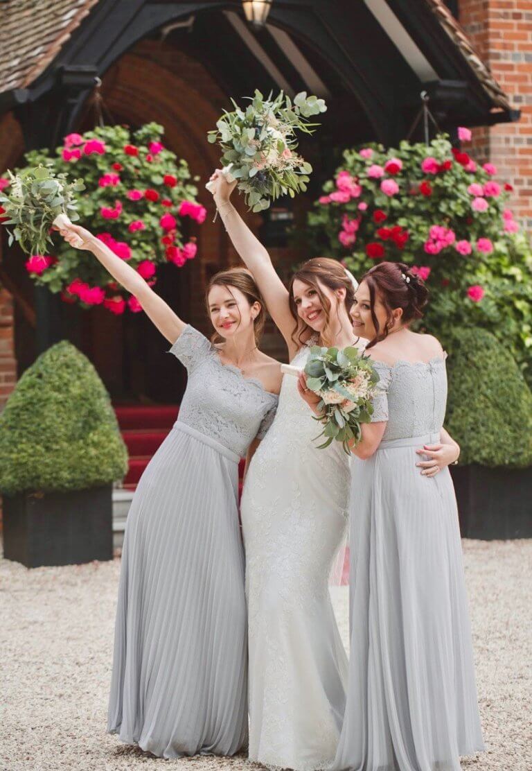 Bride and her bridesmaids raising their bouquets outside Hampshire wedding venue Careys Manor Hotel