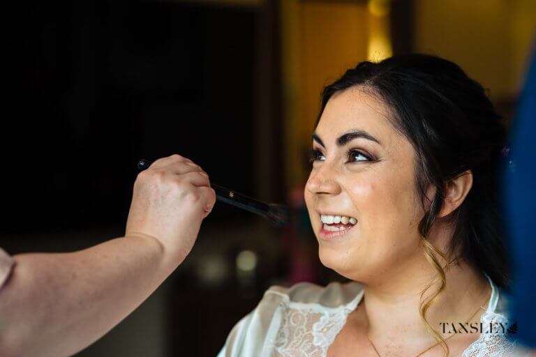 The Bride smiles as she gets her make up done before her wedding