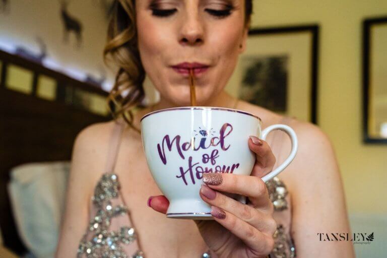 Bridesmaid drinking from a straw and tea cup which reads Maid of Honour