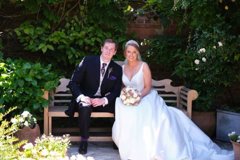 Bride and Groom pose for a photo on the bench in the garden