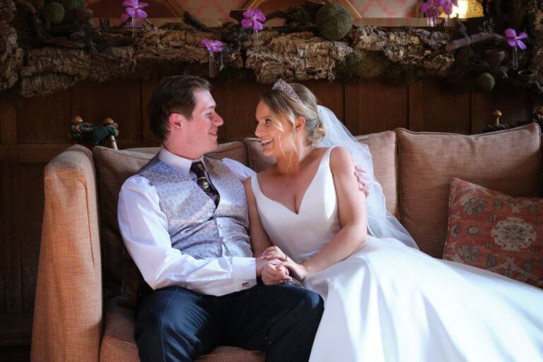 Bride and Groom smile and gaze at each other whilst relaxing on a sofa